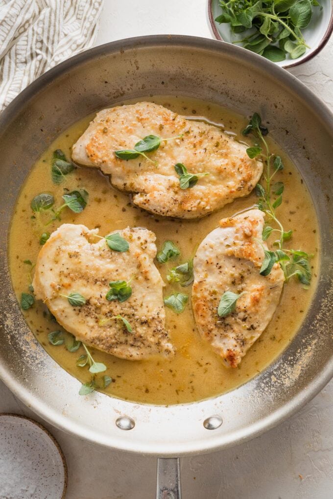 Overhead image of oregano chicken in a skillet with fresh oregano sprigs scattered around.