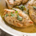 Close up of a pan-fried chicken breast seasoned with white wine sauce and oregano.