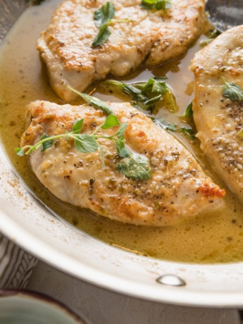Close up of a pan-fried chicken breast seasoned with white wine sauce and oregano.