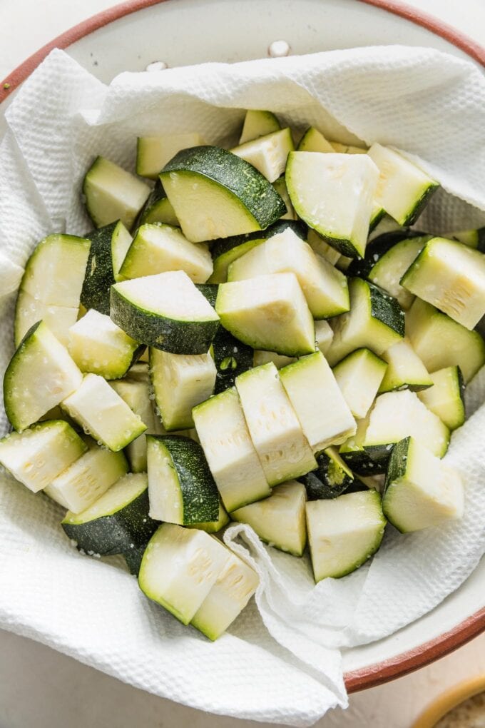 Quartered zucchini slices in a paper towel-lined bowl sprinkled with salt.