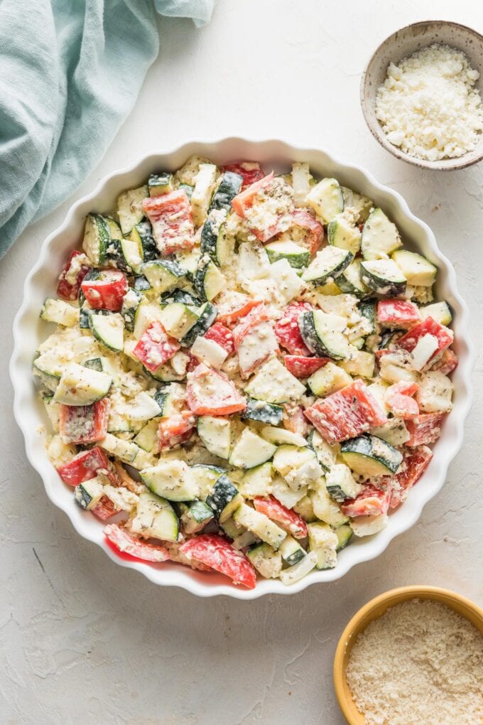 Zucchini casserole mixture spread out into a shallow white scalloped baking dish.