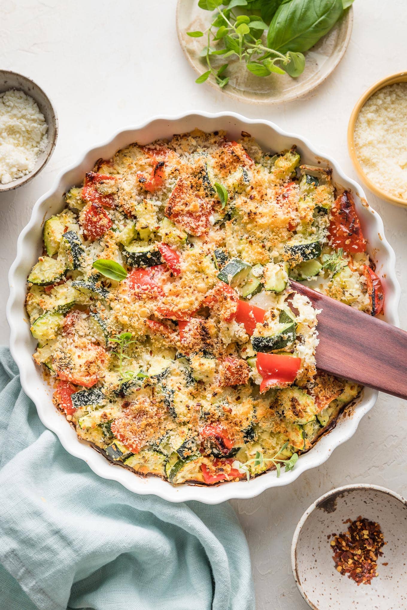 Easy zucchini casserole with red bell peppers, feta, garlic, and Parmesan, just baked in a white round baking dish with a scalloped edge.