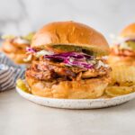 Close up of a BBQ chicken sandwich served with red cabbage coleslaw and potato chips.