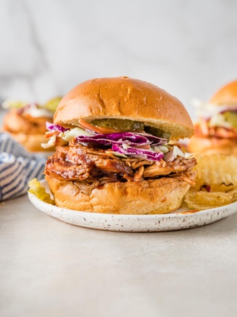 Close up of a BBQ chicken sandwich served with red cabbage coleslaw and potato chips.