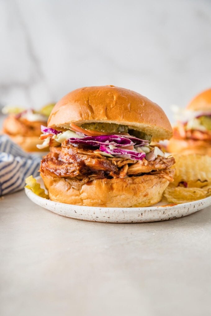 Close up of a BBQ chicken sandwich served with red cabbage coleslaw and potato chips.