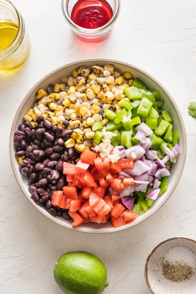 Corn, black beans, chopped bell pepper, chopped onion, and chopped tomato all piled into a bowl.
