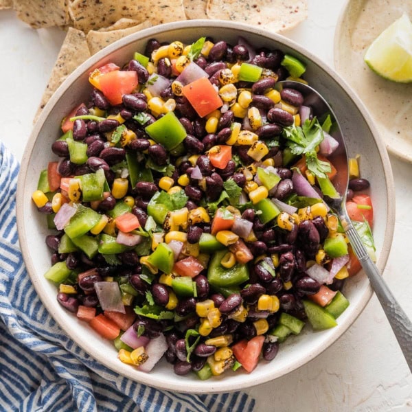 Serving bowl full of black bean salsa surrounded by tortilla chips and extra lime wedges.