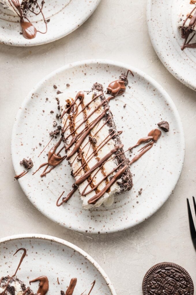 Small white plate holding a slice of Oreo ice cream cake drizzled with melted chocolate.