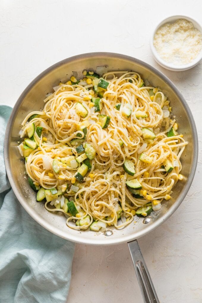 Skillet full of pasta with zucchini and corn in a light white wine butter sauce with Parmesan.