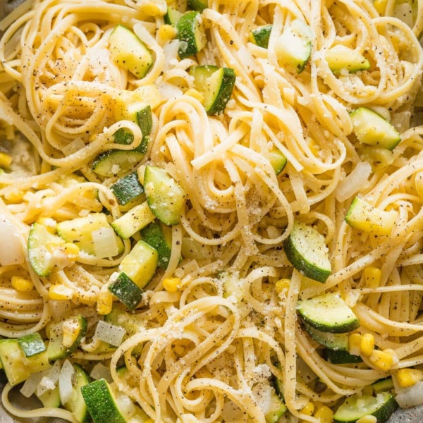 Close up of a skillet holding al dente linguine mixed with zucchini and corn in a light buttery sauce.