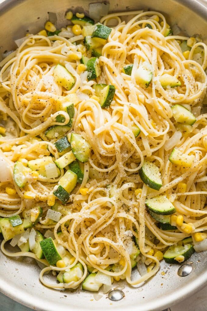 Close up of a skillet holding al dente linguine mixed with zucchini and corn in a light buttery sauce.