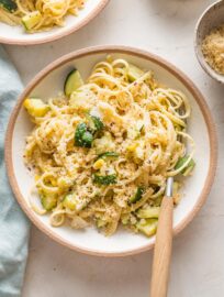 Bowl with a helping of pasta with zucchini and corns in a buttery sauce with toasted breadcrumbs on top.