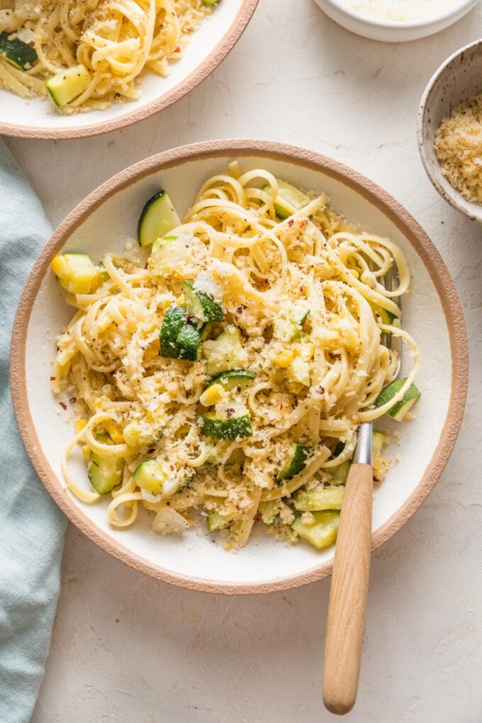 Bowl with a helping of pasta with zucchini and corns in a buttery sauce with toasted breadcrumbs on top.