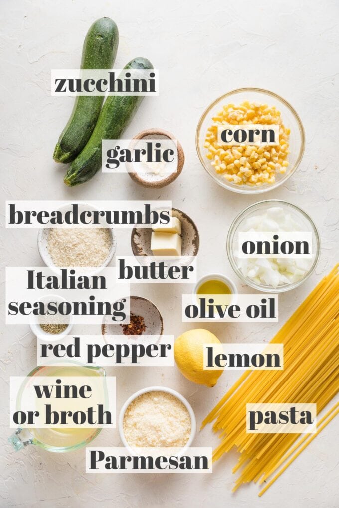 Overhead image of zucchini, corn, garlic, breadcrumbs, onion, olive oil, butter, Italian seasoning, red pepper flakes, white wine, Parmesan, lemon, and pasta arranged in prep bowls.