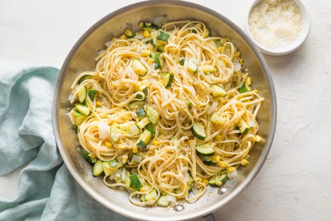 Pasta being added to and tossed with zucchini and corn in a skillet.