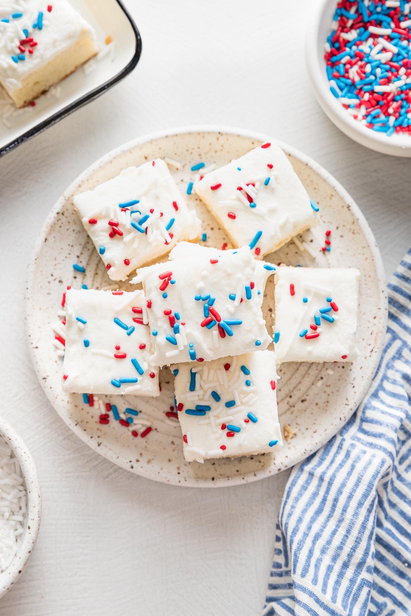Small white plate holding small sugar cookie bars decorated with white frosting and red, white, and blue sprinkles.