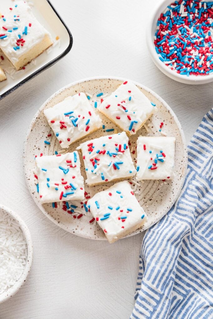 Small white plate holding small sugar cookie bars decorated with white frosting and red, white, and blue sprinkles.
