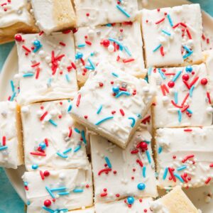 Large pile of sugar cookie bars topped with white frosting and a red, white, and blue sprinkle mix.