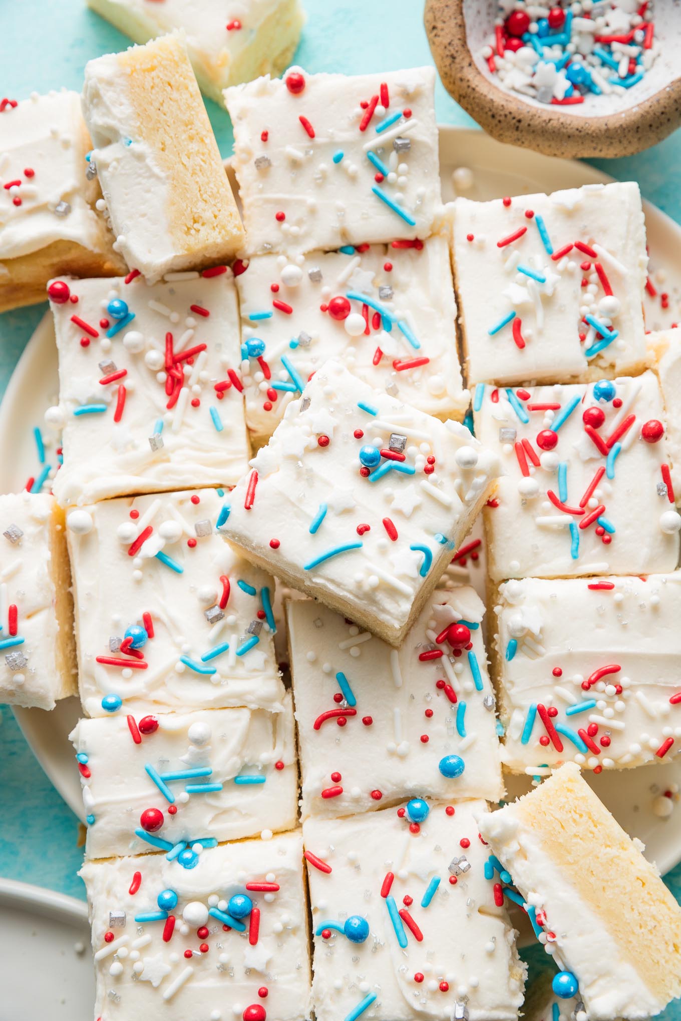 Large pile of sugar cookie bars topped with white frosting and a red, white, and blue sprinkle mix.