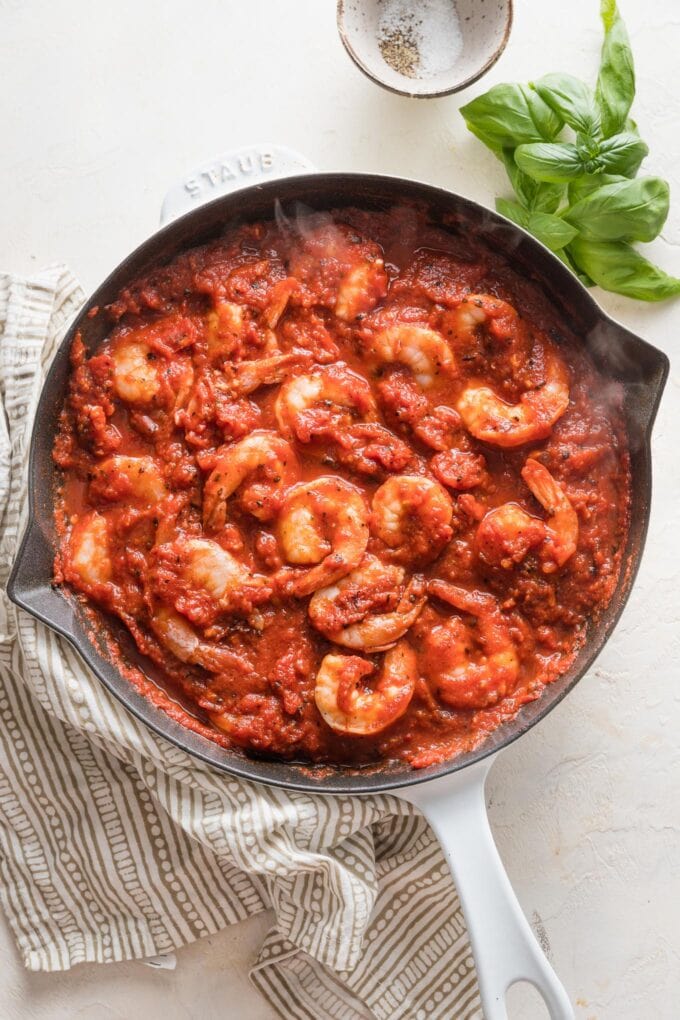 A white cast iron skillet full of cooked shrimp in homemade marinara sauce.
