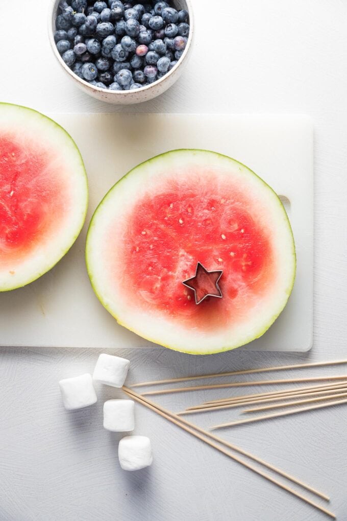 Overhead image of a slice of watermelon on a cutting board with a star cookie cutter resting on top.