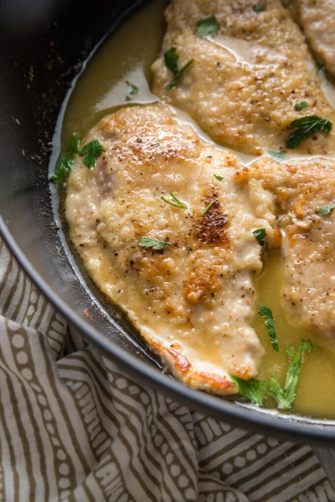 Close up of a chicken breast in white wine sauce in a deep cast iron skillet.