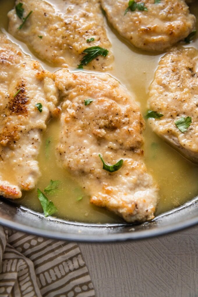 Cast iron skillet holding several chicken breasts in a light white wine sauce.
