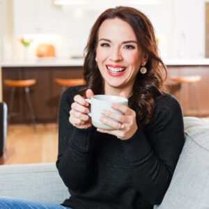 Monica Lensink sitting on her couch with a mug of coffee and the kitchen in the background.