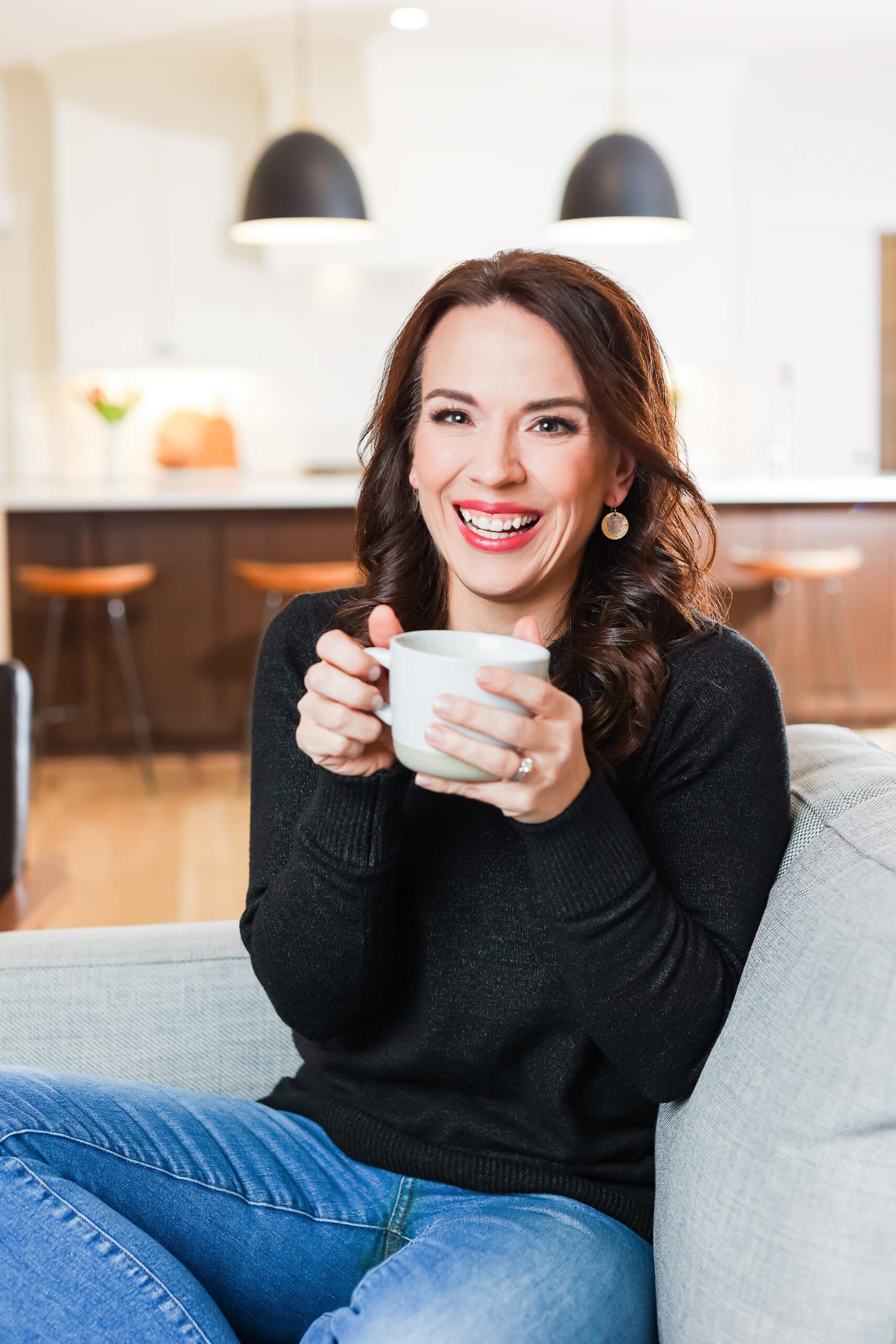 Monica Lensink sitting on her couch with a mug of coffee and the kitchen in the background.