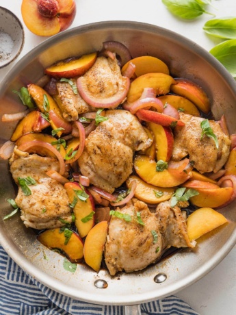 Large stainless steel skillet filled with a one pan dish of chicken thighs with sliced peaches, fresh basil, red onion, and a light balsamic glaze.