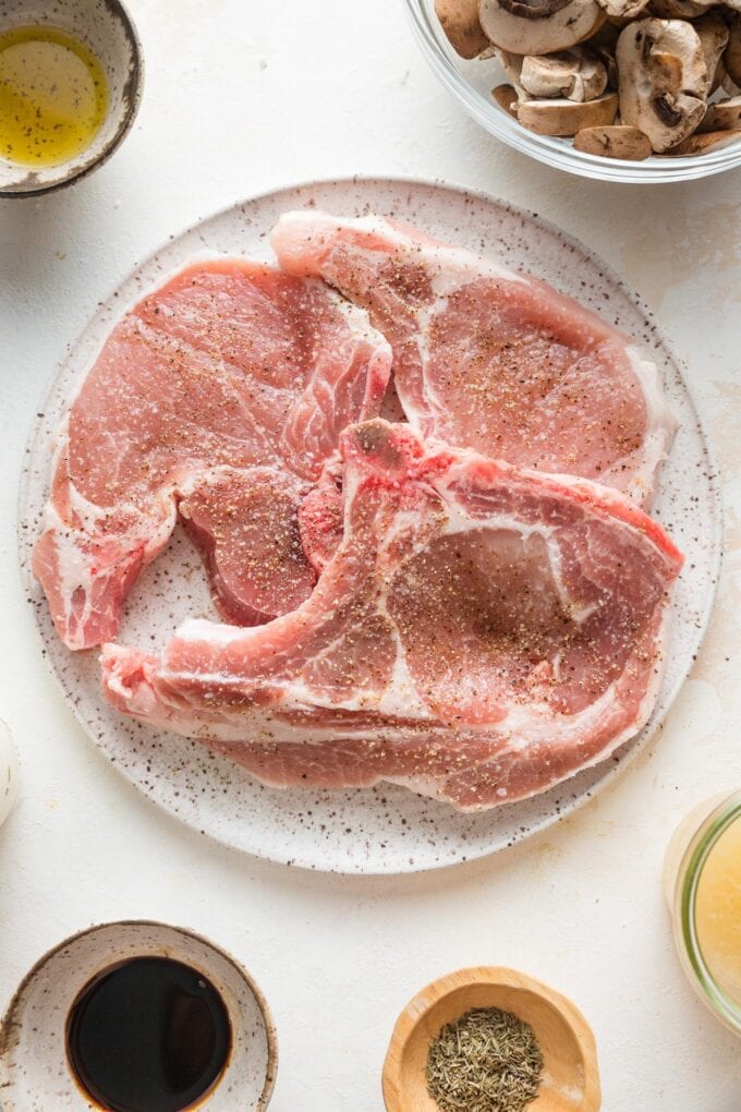 Close up of pork chops generously seasoned with kosher salt and fresh-cracked black pepper.
