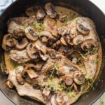 Deep cast iron skillet full of balsamic pork chops with mushrooms and a light cream sauce with fresh thyme.