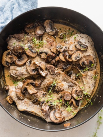 Deep cast iron skillet full of balsamic pork chops with mushrooms and a light cream sauce with fresh thyme.