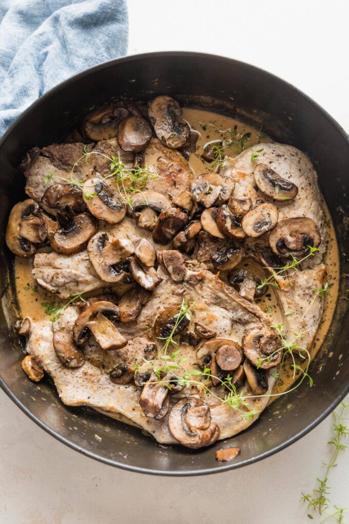 Deep cast iron skillet full of balsamic pork chops with mushrooms and a light cream sauce with fresh thyme.