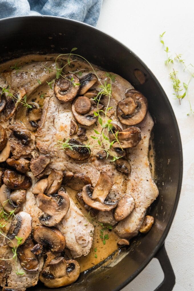 Close up of a bone-in pork chop cooked in a skillet with mushrooms and a light balsamic cream sauce.