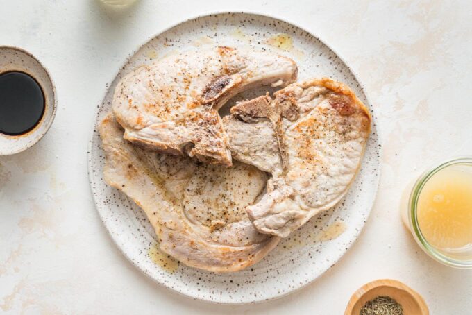 Seared bone-in pork chops removed from a skillet and placed on a plate to rest.