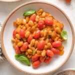 Small bowl filled with a serving of braised white beans with a light sauce and cherry tomatoes.
