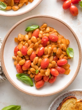 Small bowl filled with a serving of braised white beans with a light sauce and cherry tomatoes.