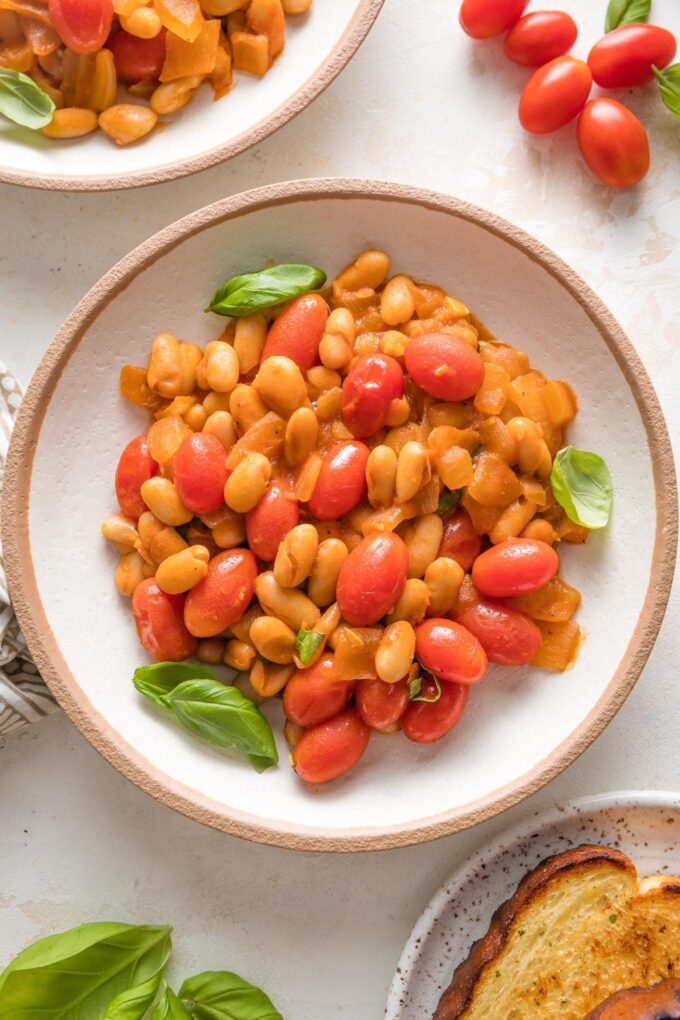 Small bowl filled with a serving of braised white beans with a light sauce and cherry tomatoes.