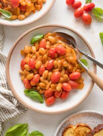 Small bowl with a fork and spoon filled with a serving of braised white beans with a light sauce and cherry tomatoes.