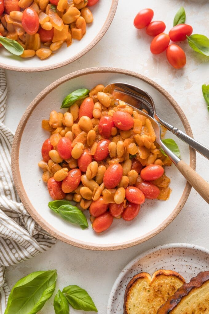 Small bowl with a fork and spoon filled with a serving of braised white beans with a light sauce and cherry tomatoes.