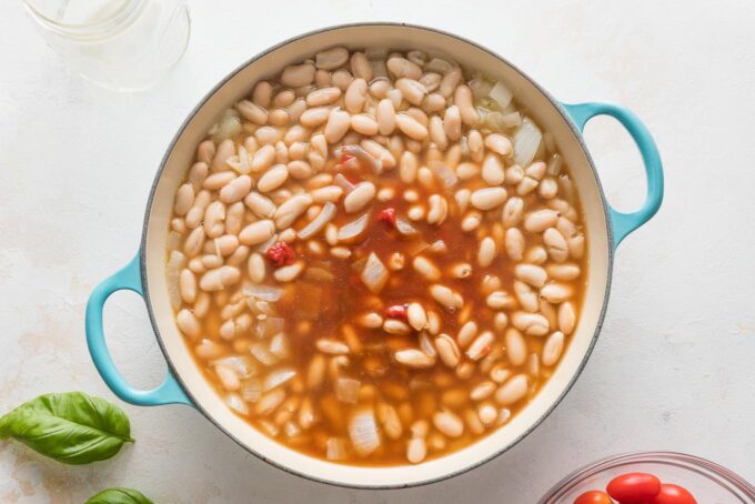 Skillet with onion, cannellini beans, broth, tomato paste, and balsamic vinegar combining into a sauce.