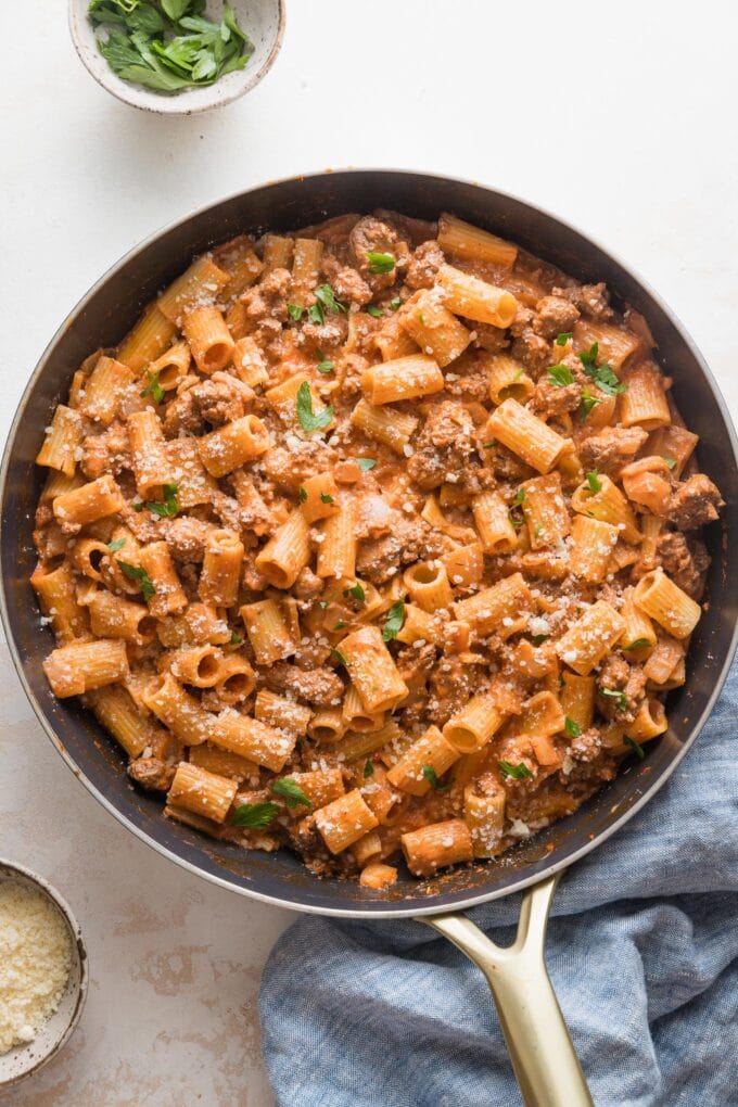 Large skillet filled with a simple ground beef pasta dish garnished with Parmesan cheese and fresh parsley.