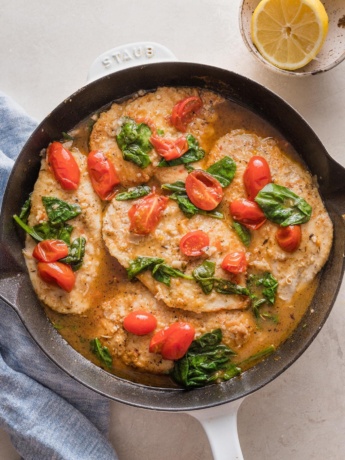 Cast iron skillet filled with chicken breasts in a light white wine sauce with spinach and tomatoes.