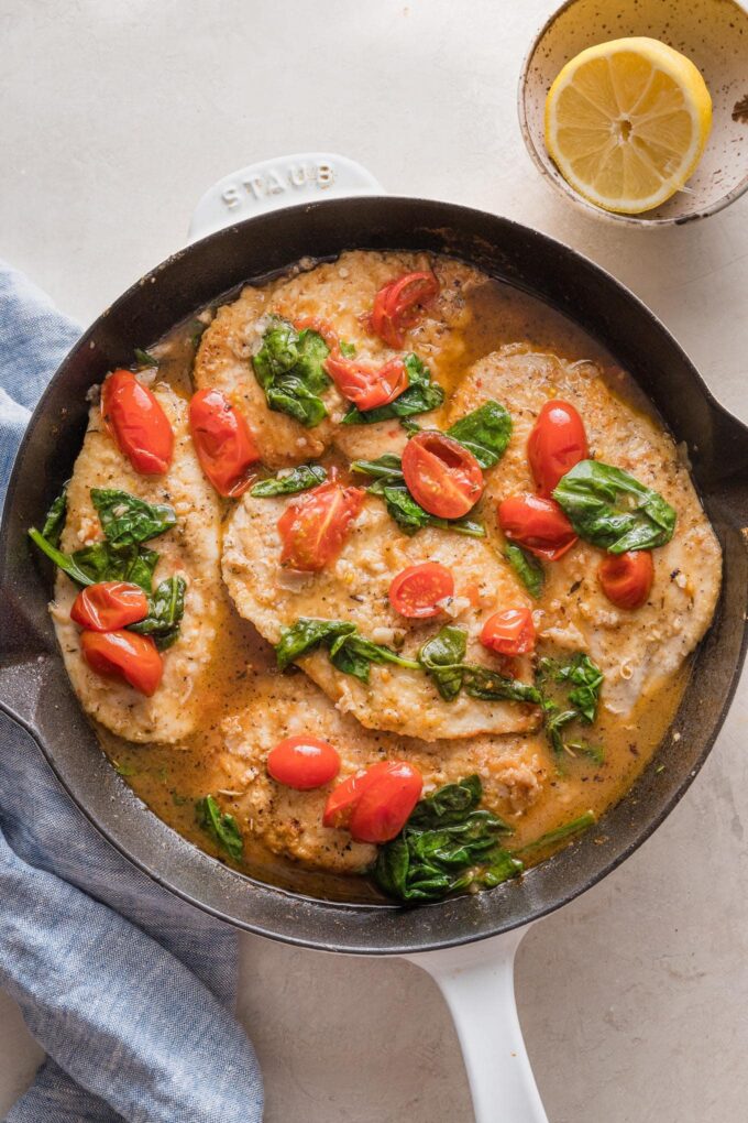 Cast iron skillet filled with chicken breasts in a light white wine sauce with spinach and tomatoes.