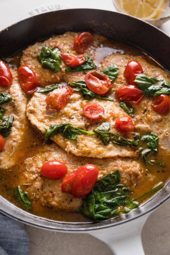 Close up of a cast iron skillet full of white wine chicken with baby spinach and burst cherry tomatoes.