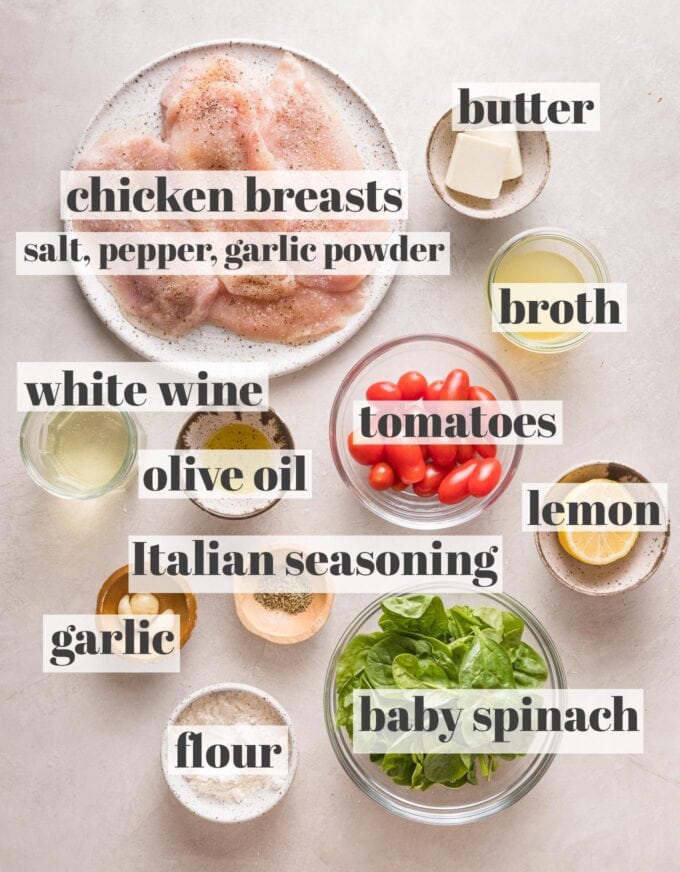 Labeled overheat image of chicken breasts seasoned with salt, pepper, and garlic powder; butter; olive oil; broth; white wine; cherry tomatoes; baby spinach; flour, garlic cloves; and Italian seasoning measured into prep bowls and ready to cook.