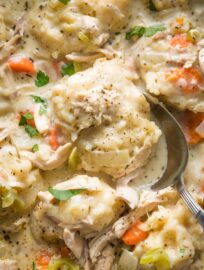 Close up of a serving spoon lifting a helping of chicken and dumplings out of a cast iron skillet.