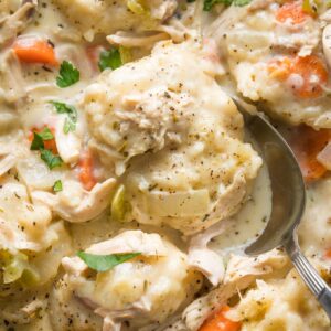 Close up of a serving spoon lifting a helping of chicken and dumplings out of a cast iron skillet.