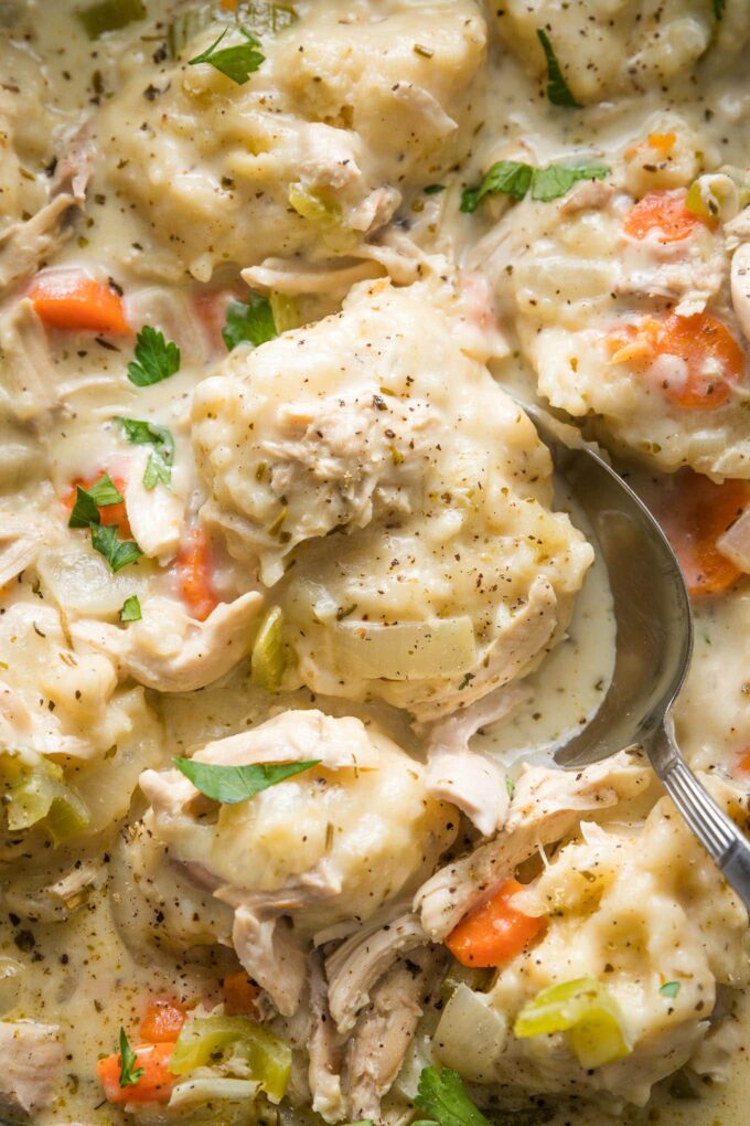 Close up of a serving spoon lifting a helping of chicken and dumplings out of a cast iron skillet.